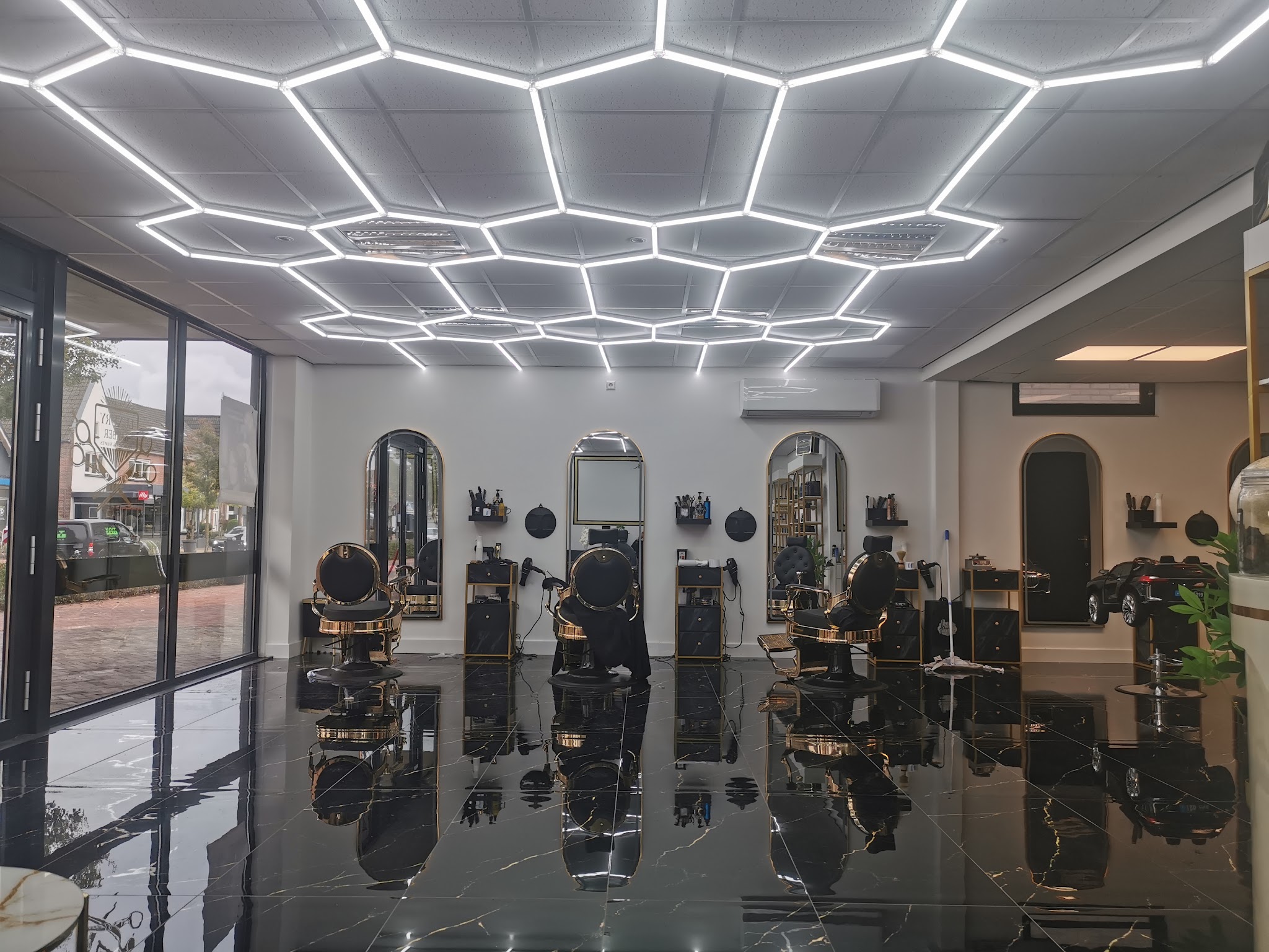De zaak van binnen: verlicht plafond, boogspiegels, gouden stoelen en een glanzende zwart marmeren vloer